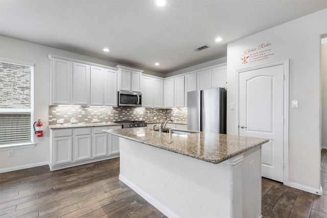 kitchen with visible vents, an island with sink, light stone counters, stainless steel appliances, and white cabinetry