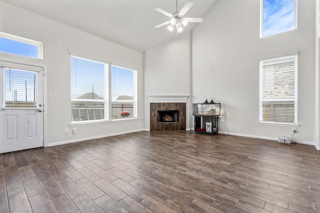 unfurnished living room with baseboards, ceiling fan, dark wood-type flooring, a fireplace, and high vaulted ceiling