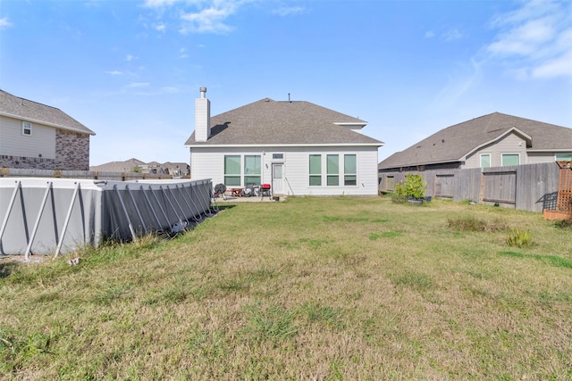 rear view of property featuring a pool, a yard, a chimney, and fence