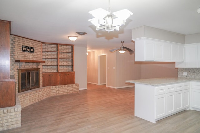 kitchen featuring a peninsula, a fireplace, white cabinetry, light wood-style floors, and open floor plan