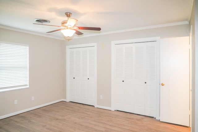 unfurnished bedroom with visible vents, baseboards, ornamental molding, light wood-type flooring, and two closets