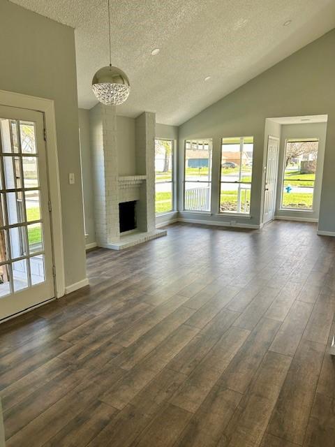 unfurnished living room featuring baseboards, dark wood finished floors, lofted ceiling, a textured ceiling, and a brick fireplace