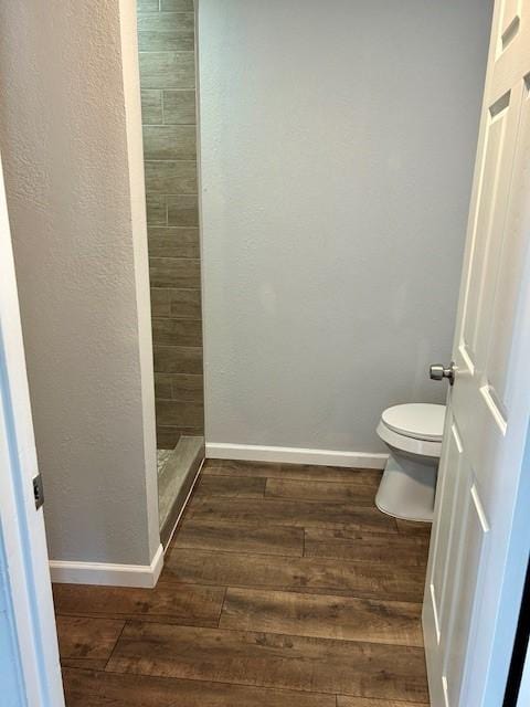 full bath featuring toilet, a shower stall, baseboards, and wood finished floors