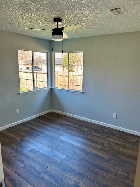 empty room featuring a ceiling fan, visible vents, dark wood finished floors, and baseboards