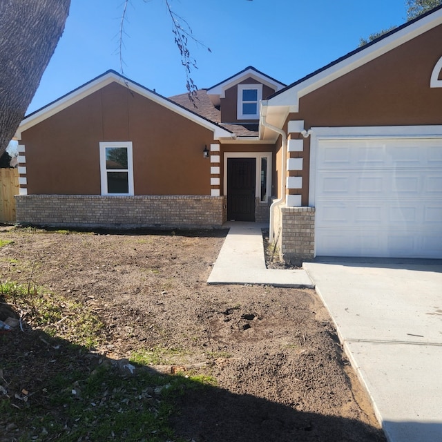 view of front facade with an attached garage, stucco siding, driveway, and brick siding