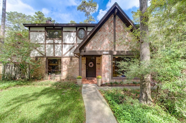 tudor-style house with brick siding, a chimney, and a front lawn