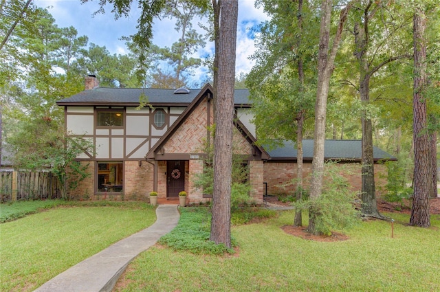 tudor house featuring stucco siding, fence, a front yard, brick siding, and a chimney