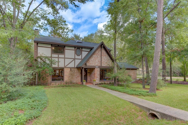 english style home featuring stucco siding, a front yard, a shingled roof, brick siding, and a chimney