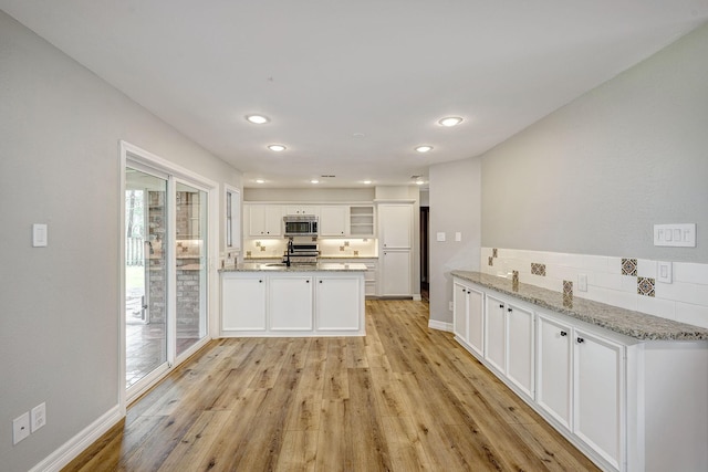 kitchen featuring light wood-type flooring, a sink, stainless steel appliances, a peninsula, and white cabinets