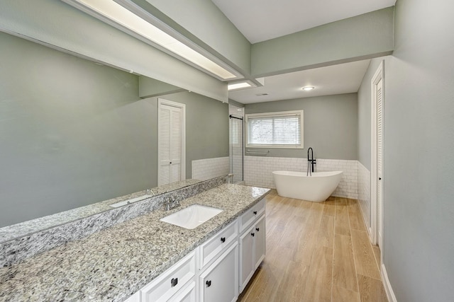 bathroom with wood finished floors, vanity, wainscoting, a freestanding tub, and tile walls