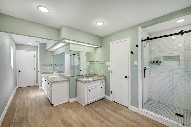 bathroom with a sink, wood finished floors, two vanities, and a stall shower