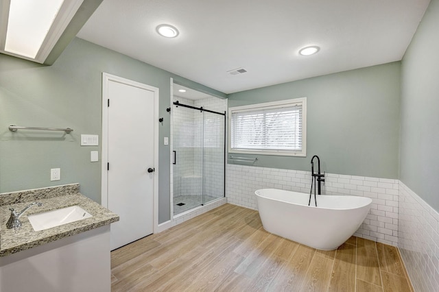 full bath featuring visible vents, a shower stall, wood finished floors, a freestanding tub, and tile walls