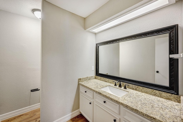 bathroom featuring a textured wall, vanity, baseboards, and wood finished floors