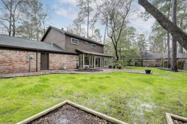 back of house featuring brick siding, a lawn, and fence