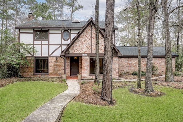 english style home featuring a front yard, a shingled roof, stucco siding, a chimney, and brick siding