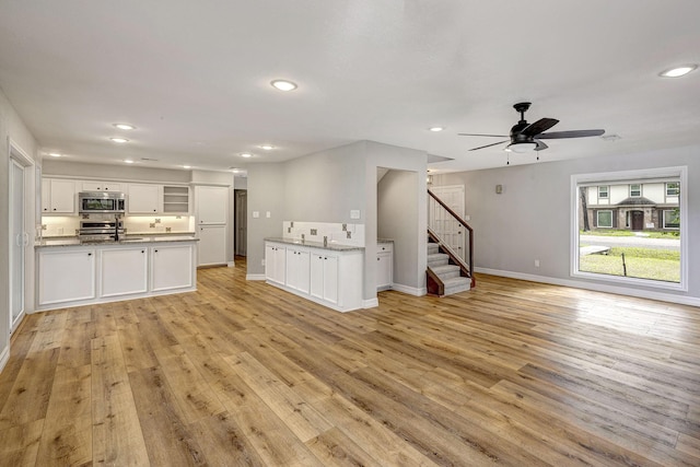 unfurnished living room featuring light wood finished floors, baseboards, stairs, recessed lighting, and a sink