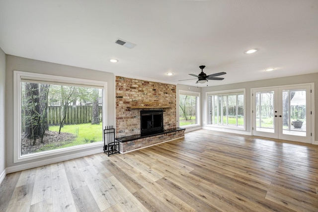 unfurnished living room with hardwood / wood-style flooring, a brick fireplace, visible vents, and a wealth of natural light