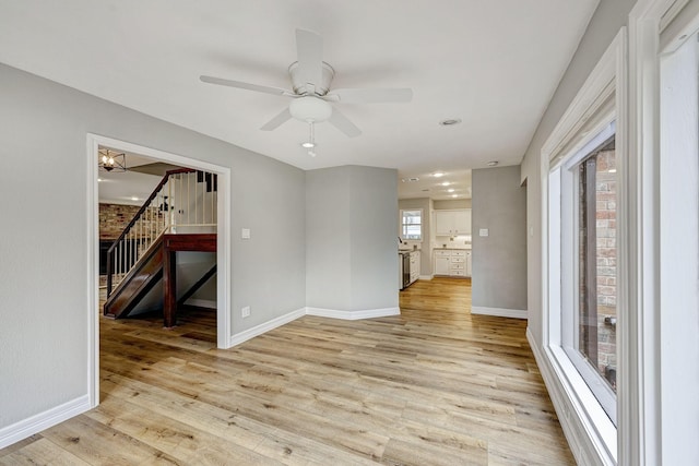 spare room featuring light wood finished floors, stairway, a ceiling fan, and baseboards