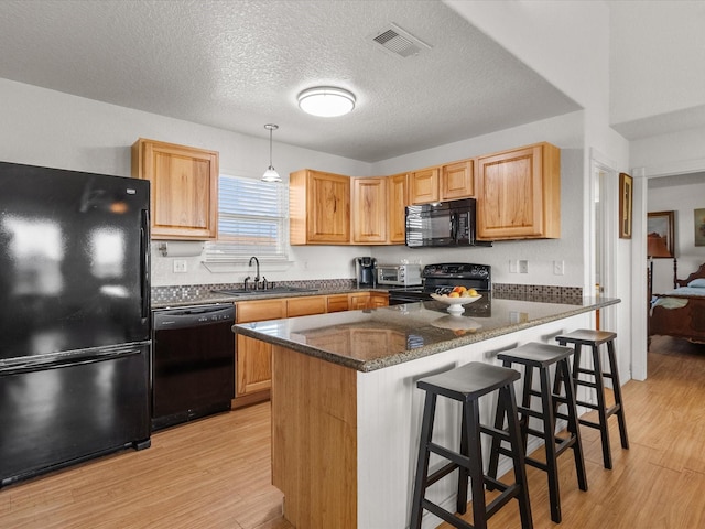 1206 Middle Dr W, Surfside Beach, TX 77541 - kitchen with black appliances, light wood-style flooring, dark stone countertops, a peninsula, and a kitchen bar