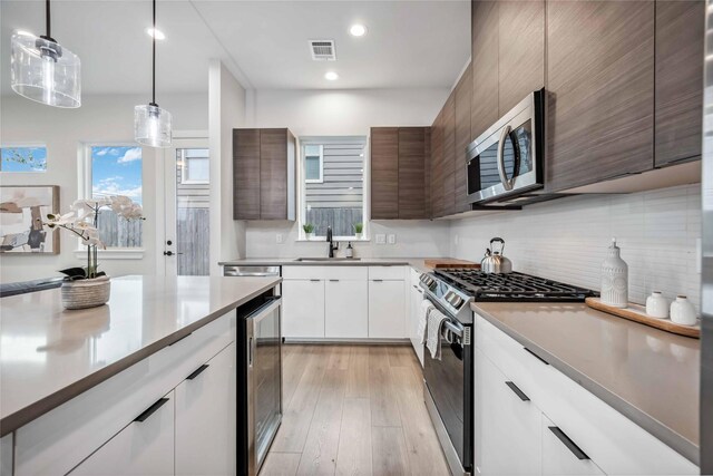 kitchen featuring modern cabinets, stainless steel appliances, light wood-style floors, white cabinetry, and a sink