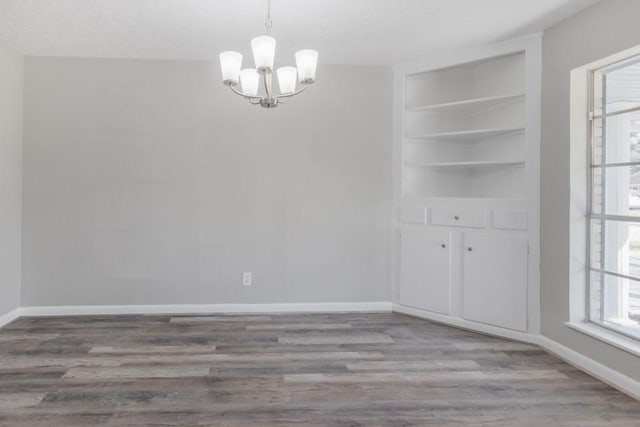 unfurnished dining area with baseboards, a notable chandelier, and wood finished floors
