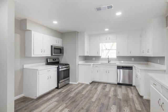 kitchen with visible vents, light wood-style flooring, a sink, stainless steel appliances, and white cabinets