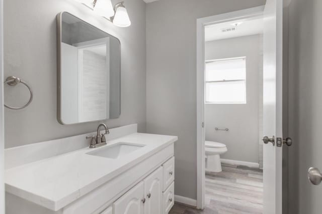 bathroom featuring visible vents, toilet, wood finished floors, baseboards, and vanity