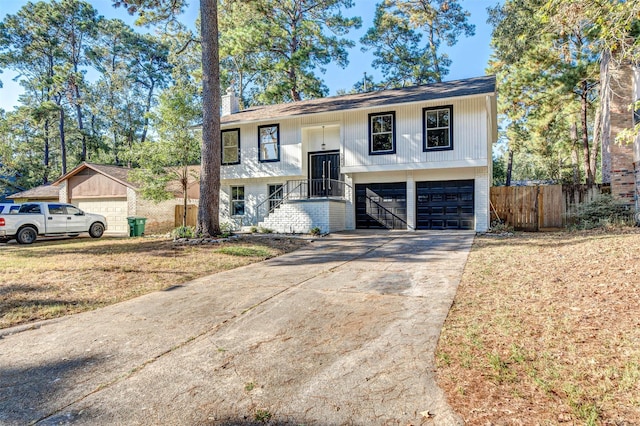 bi-level home featuring driveway, a chimney, an attached garage, fence, and brick siding