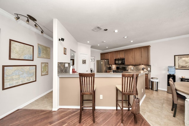 kitchen with visible vents, a breakfast bar, a peninsula, light countertops, and black appliances