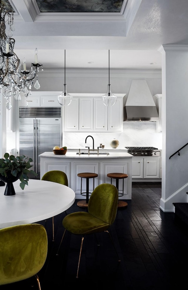 kitchen featuring wall chimney range hood, crown molding, stainless steel built in refrigerator, and a sink