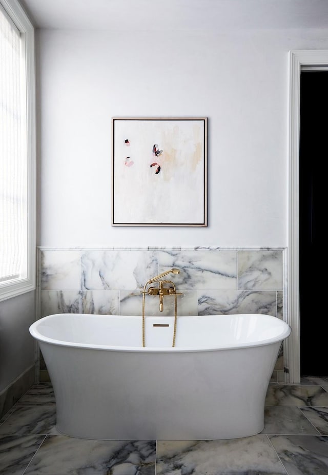 full bathroom with a freestanding bath, marble finish floor, and wainscoting