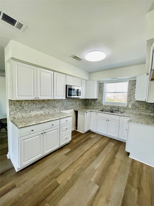 kitchen with light wood finished floors, stainless steel microwave, visible vents, white cabinets, and a sink