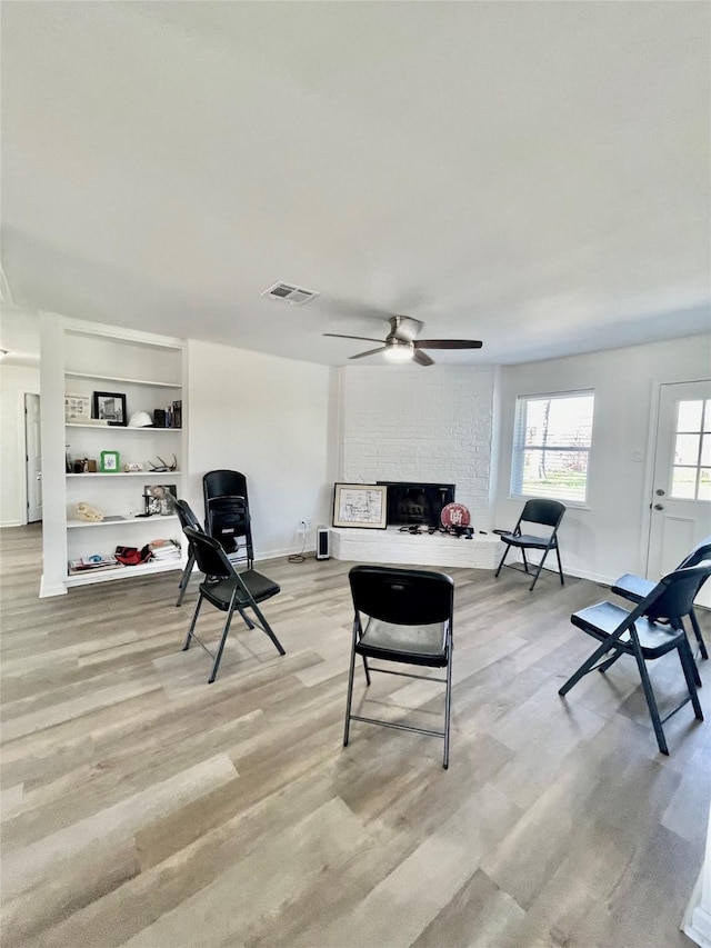 living room featuring a ceiling fan, a fireplace, visible vents, and light wood-style floors