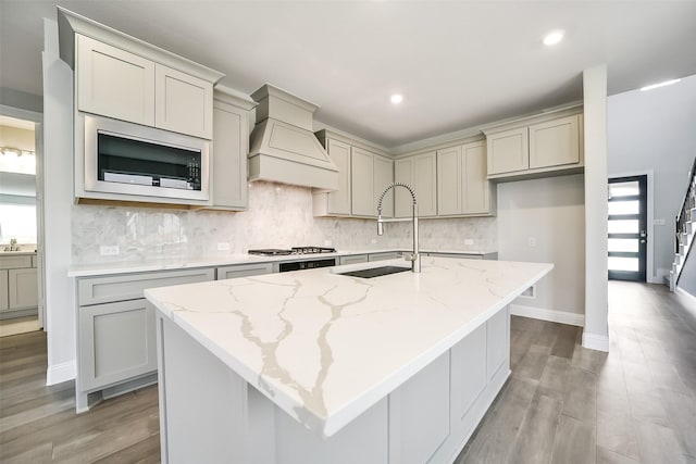 16319 Placid Stream St, Conroe, TX 77302 - kitchen with a sink, built in microwave, premium range hood, light stone counters, and decorative backsplash