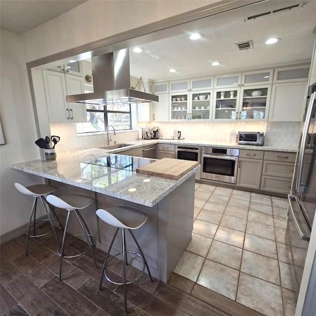kitchen featuring stainless steel appliances, a peninsula, island exhaust hood, tasteful backsplash, and visible vents