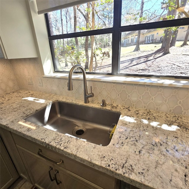 details featuring light stone counters, a sink, and backsplash