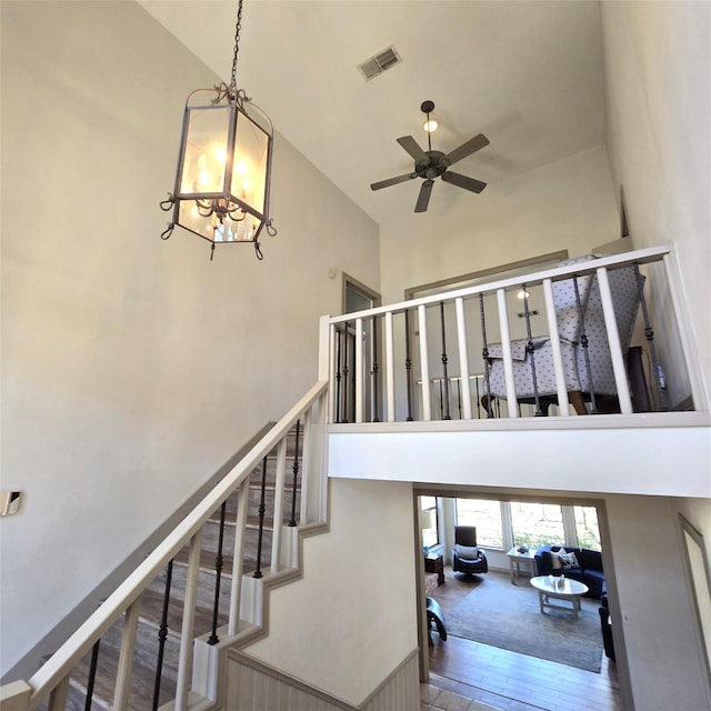 stairs with visible vents, ceiling fan with notable chandelier, and a towering ceiling