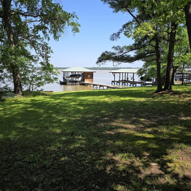 dock area with boat lift, a water view, and a yard