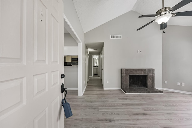 entrance foyer with lofted ceiling, visible vents, light wood finished floors, and a tiled fireplace