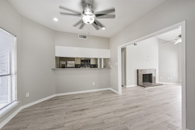 unfurnished living room featuring light wood finished floors, baseboards, visible vents, a ceiling fan, and a fireplace