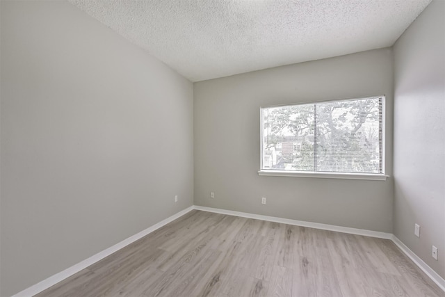 spare room featuring a textured ceiling, light wood-type flooring, and baseboards