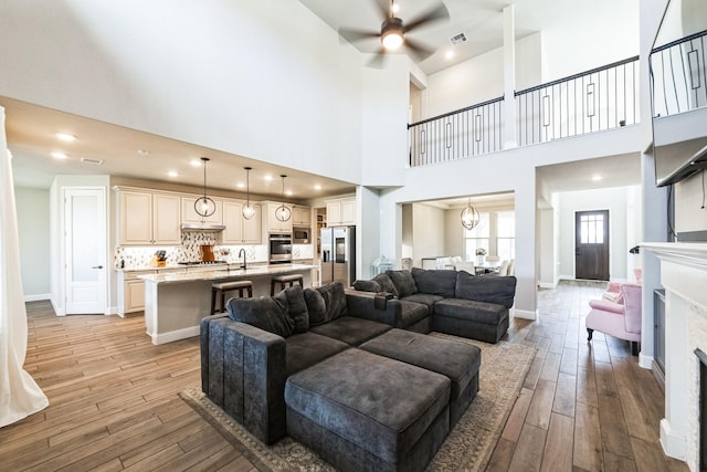 living area featuring light wood-style floors, a fireplace, baseboards, and ceiling fan with notable chandelier