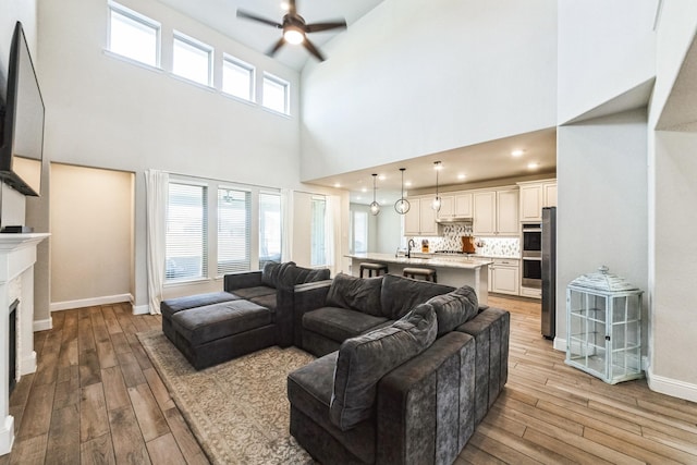 living area with a ceiling fan, a fireplace, light wood-style flooring, and baseboards