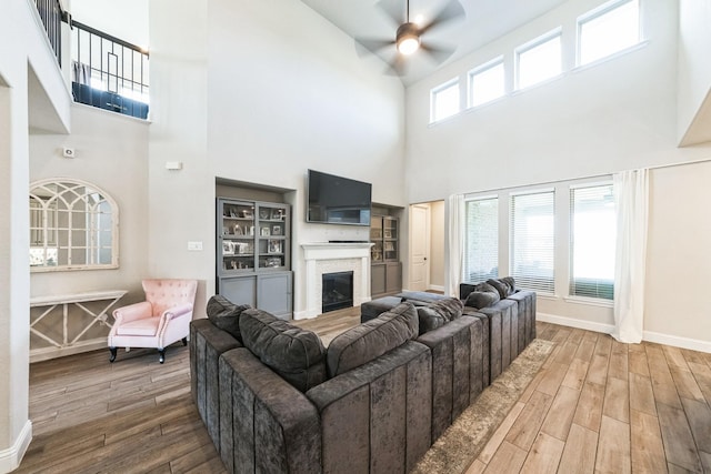 living room with ceiling fan, a glass covered fireplace, wood finished floors, and baseboards