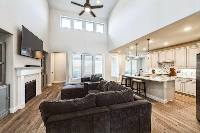 living room with light wood-type flooring, a fireplace, a ceiling fan, and baseboards