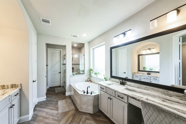 full bathroom featuring a garden tub, two vanities, visible vents, a stall shower, and a sink