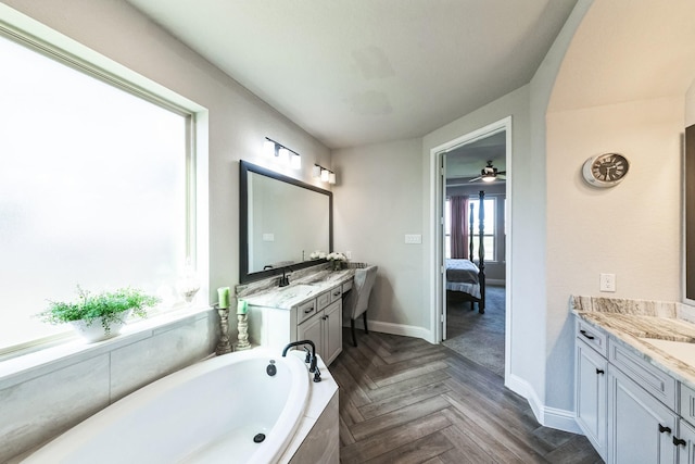 full bath featuring connected bathroom, baseboards, two vanities, and a bath