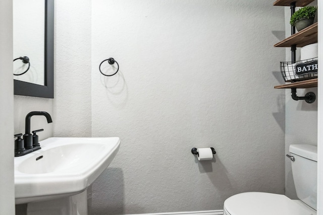 half bathroom with a textured wall, baseboards, a sink, and toilet