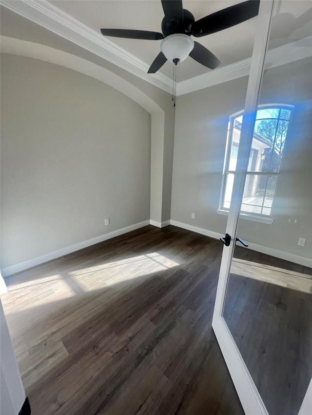 empty room with ceiling fan, ornamental molding, dark wood-type flooring, and baseboards