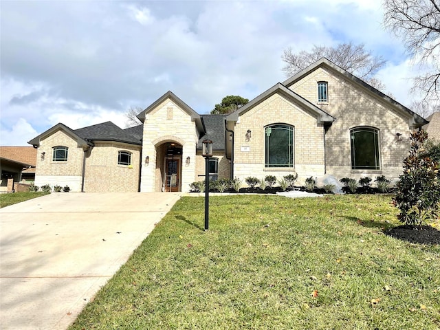 french provincial home with stone siding, concrete driveway, brick siding, and a front lawn